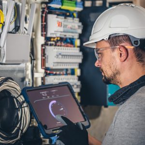 Man, an electrical technician working in a switchboard with fuses, uses a tablet.